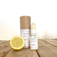 Lemon Breeze vaskeduft indpakning og flacon på et ældre tømmerbord, lys baggrund og en halv citron ved siden af