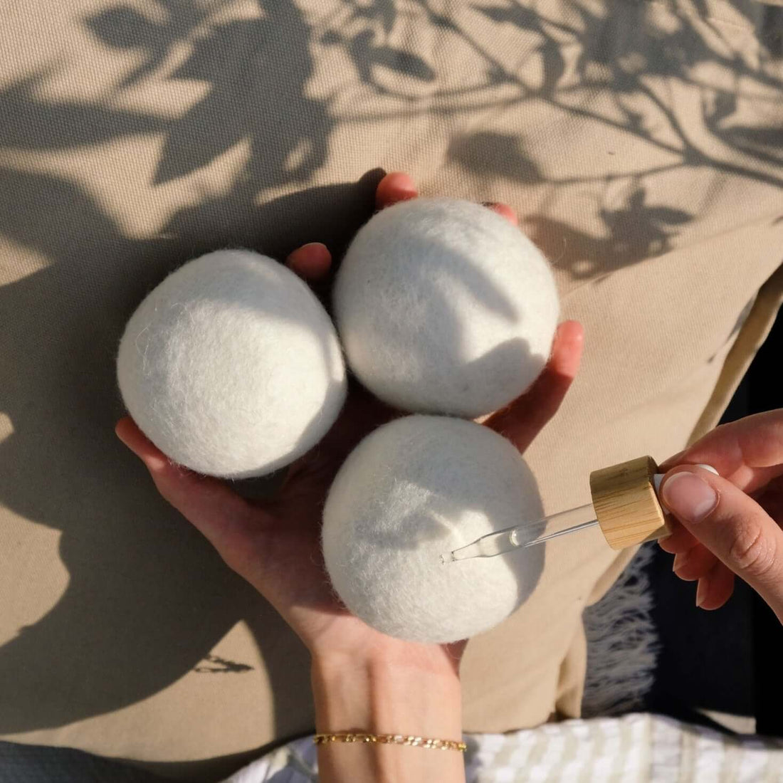 3 Care by nature tørrebolde til tørretumbler der holdes i en hånd, hvor den anden hånd drypper vaskeduft på fra en pippette på naturlig beige baggrund med skygger af planter fra solens naturlige stråler